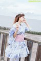 A woman in a blue and pink kimono standing on a wooden railing.