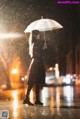 A woman standing in the rain holding an umbrella.