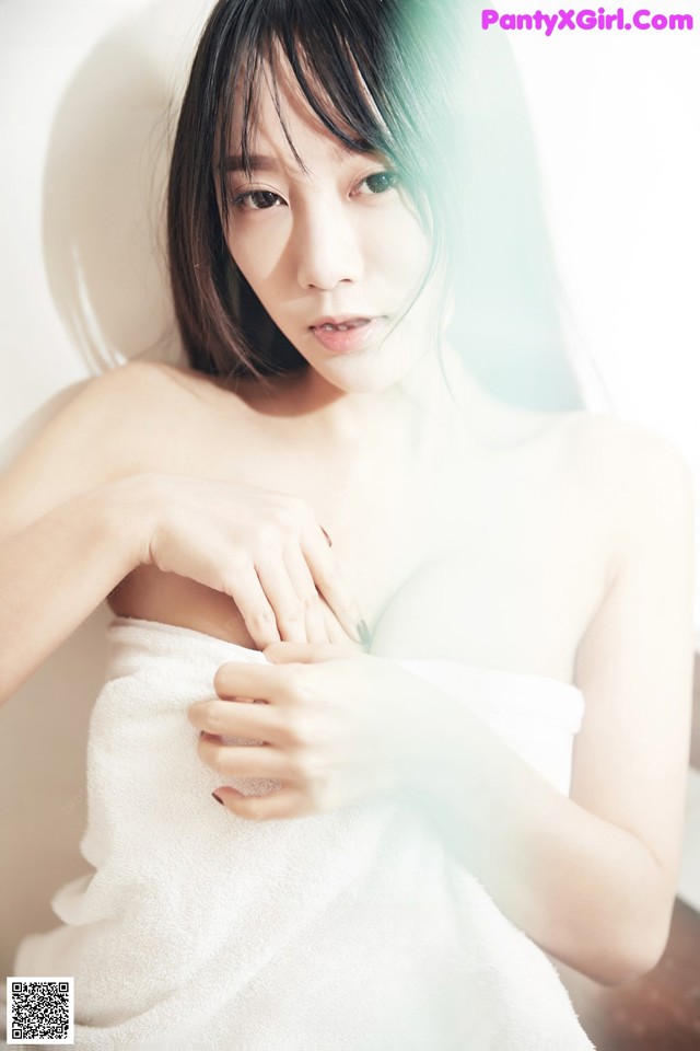 A woman wrapped in a white towel sitting in a bathtub.